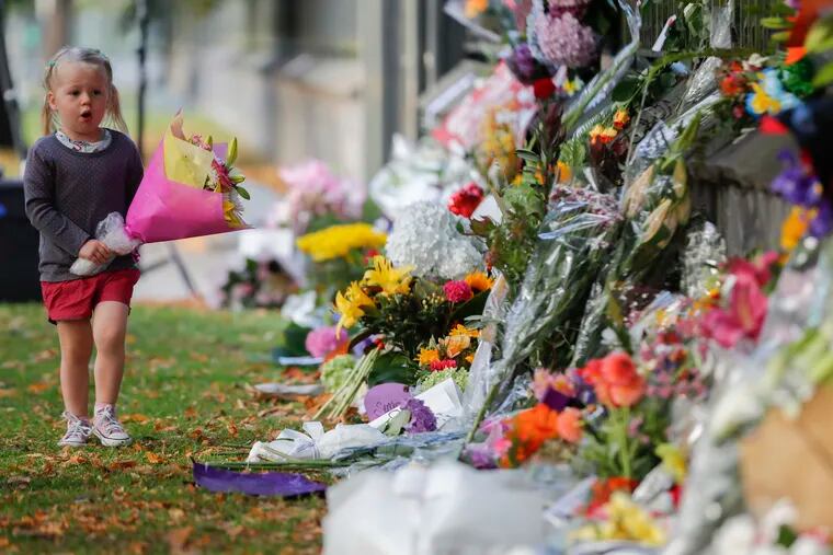 A girl walk to lay flowers on a wall at the Botanical Gardens in Christchurch, New Zealand, Sunday, March 17, 2019. New Zealand's stricken residents reached out to Muslims in their neighborhoods and around the country on Saturday, in a fierce determination to show kindness to a community in pain as a 28-year-old white supremacist stood silently before a judge, accused in mass shootings at two mosques that left dozens of people dead. (AP Photo/Vincent Thian)