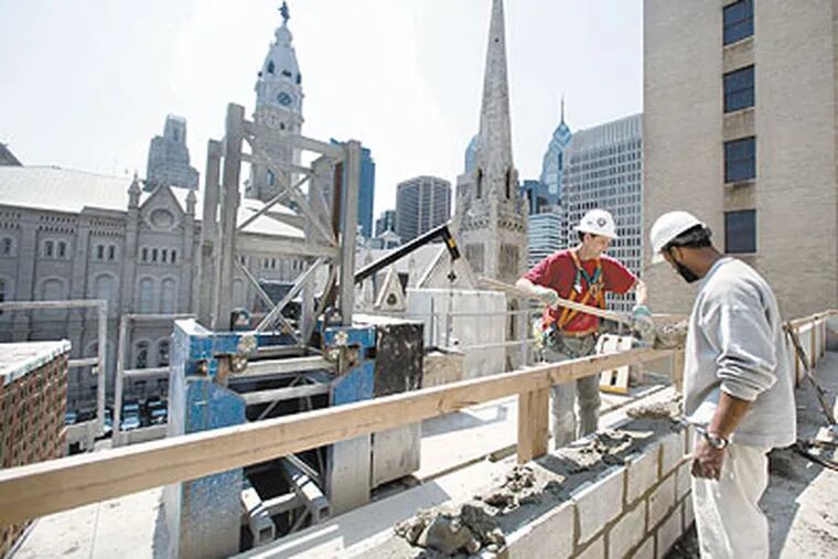 Scott Bortman, left, hauls cement to bricklayer Brian Wyatt, right, as the two work on a roof section of the Pennsylvania Convention Center overlooking City Hall and Center City. (Ed Hille / Staff Photographer)