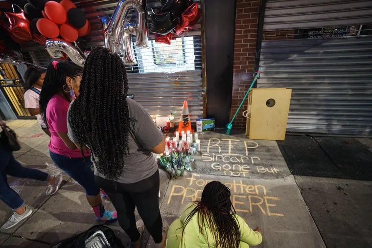 People gather on the sidewalk after a balloon release in memory of Sircarr Johnson Jr., who was fatally shot on July 4 inside his newly-opened store, Premier Bande.