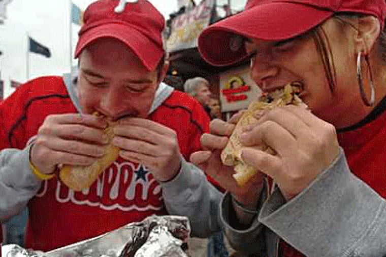 Two Phillies fans enjoy a meal from Rick's cheesesteak in Ashburn Alley, in this file photo.  (Clem Murray / Inquirer)