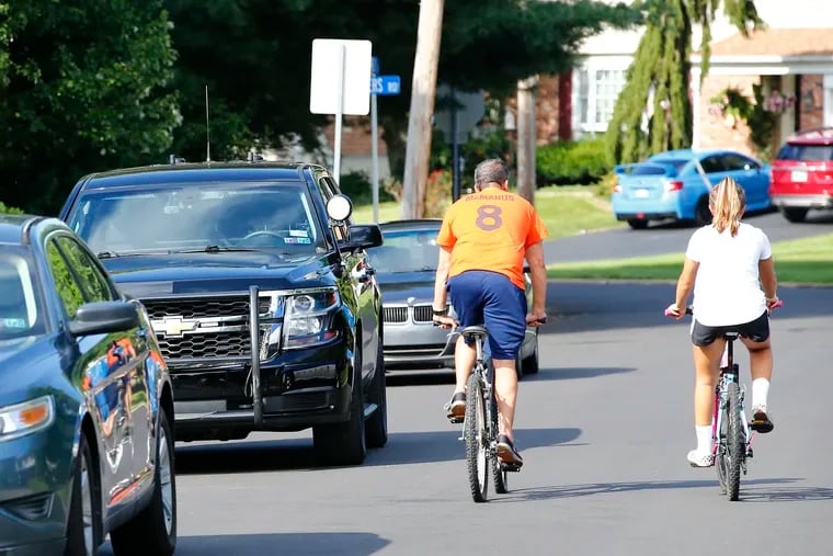 Bicyclists pass police vehicles on Cathys Lane in Upper Gwynedd Township, Montgomery County Sunday, where police said a man fired a shotgun at officers who confronted him for roaming through yards and trying to get into sheds and cars. No officers were injured. The suspect is in custody.