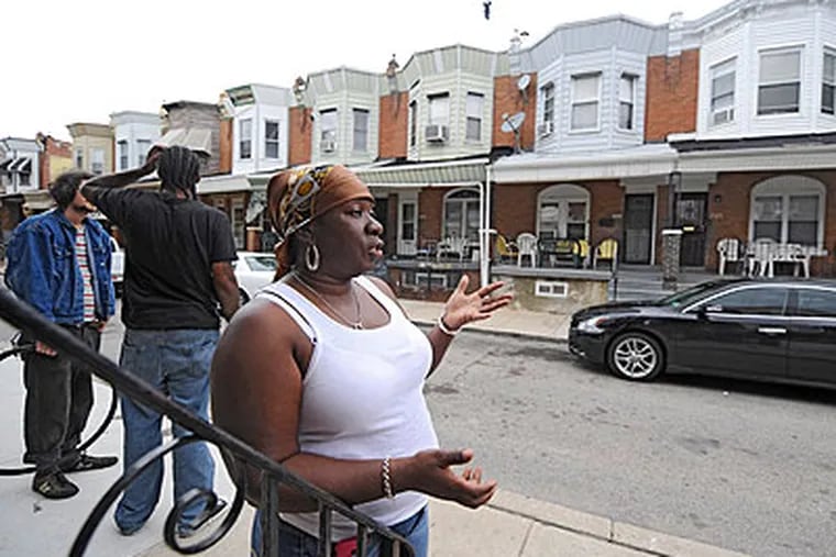 Neighbors, including Karen Mobley, congregate across the street from Corey White's family home (the one with the gold-colored chairs on the porch by her left hand) in the 5100 block of Webster Street, which is two blocks from where White was murdered overnight on Hadfield Street. (Clem Murray / Staff Photographer)