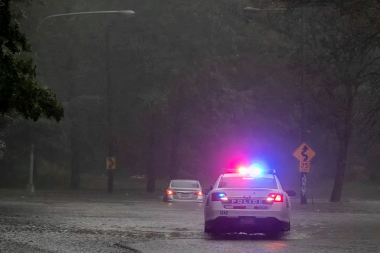 Philadelphia police officer blocks the roadway along Cobbs Creek Parkway as a vehicle sits in flood water near Springfield Ave in Philadelphia during heavy rain on August 4.