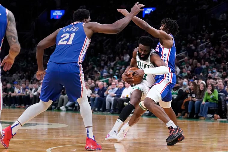 Boston Celtics guard Jaylen Brown, center, threads between Philadelphia 76ers guard Tyrese Maxey, right, and center Joel Embiid (21) on a drive to the basket during the first half of an NBA basketball game, Wednesday, Dec. 1, 2021, in Boston.