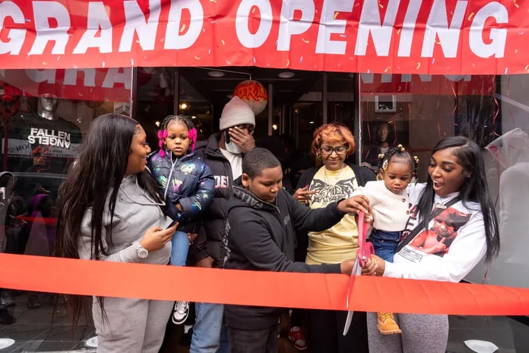From left: Samika Johnson, Sanely Johnson, Sircarr Johnson Sr., Sakai Nock, Pamela Owensby, Solei Johnson and Washika Reid cut the ribbon at the grand opening of Premiére Bande on South Street in Philadelphia on Saturday. Sircarr Johnson Jr., 23, was fatally shot in front of his clothing store in West Philadelphia in July.