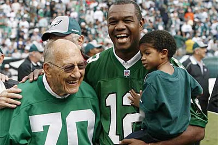 Randall Cunningham holds his son, Christian, during halftime of an Eagles game in '09. Ex-Eagle Al Wistert on left. ( David Maialetti / Staff Photographer)
