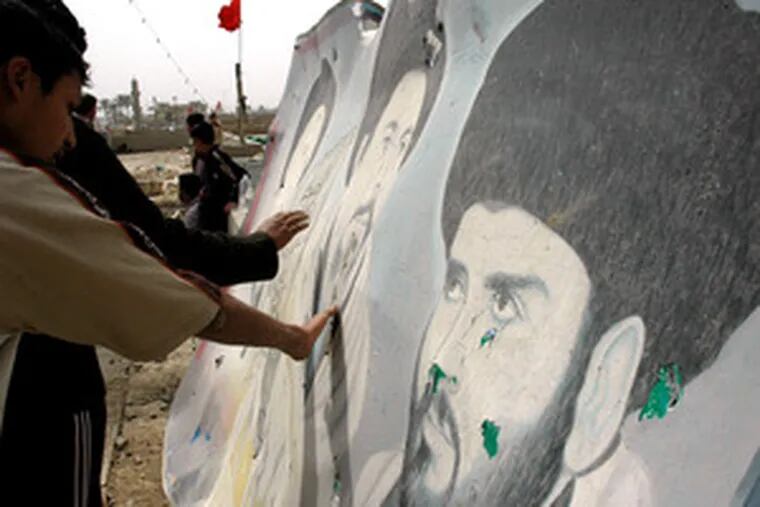 People touch a damaged poster of Muqtada al-Sadr (right) and the late Mohammed Baqir al-Sadr at a mosque in Haswa, where a suicide bomber killed 11 last week.