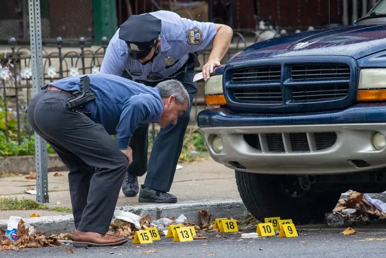 A detective and an officer looking at evidence under and around a blue SUV. Philadelphia police investigate and gather evidence at what came out as a quadruple shooting at intersection of N. 38th and Aspen in Mantua section of city on Thursday. Police have made no statements or number count on victims.