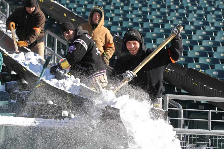 Michael Milln, of Philadelphia, uses a wooden broom to push the snow out of a slide and onto Lincoln Financial Field so it can be picked up by a front loader and taken outside. ( MICHAEL BRYANT / Staff Photographer )