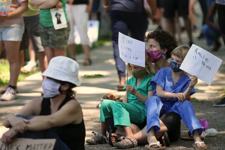 Anna Brickman sits with her twin daughters, Lilly, 6, right, and Mira, during a rally for justice for George Floyd and victims of police brutality, geared towards families and children, inside Clark Park in West Philadelphia on Tuesday, June 09, 2020. Brickman said it was "dress like an essential worker day" at Penn Alexander school, which is why they were wearing scrubs.