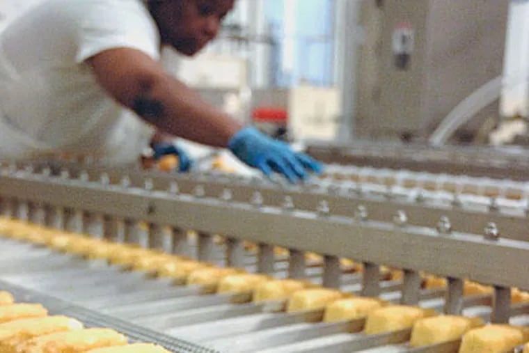 A factory worker reaches over Krimpets as they go through the production line at the new Tastykake Factory in Philadelphia on Monday. (Caroline Morris / Staff Photographer)