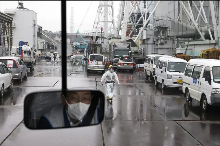 A worker wearing protective gear is seen through a tour bus window at the Fukushima Daiichi nuclear plant in Japan.
