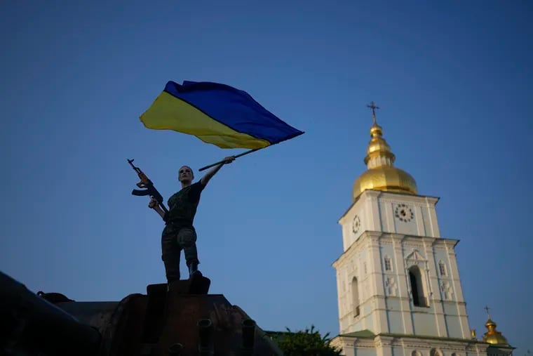 A woman brandishes the Ukrainian flag on top of a destroyed Russian tank in Kyiv, Ukraine, in June.