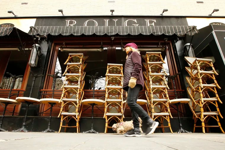 A pedestrian walks past stacks of chairs and tables in front of the restaurant Rouge in Rittenhouse Square.
