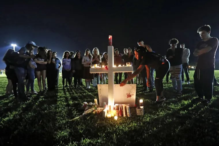 A woman places a poster of shooting victim Meadow Pollack, at one of seventeen crosses, after a candlelight vigil for the victims of the Wednesday shooting at Marjory Stoneman Douglas High School, in Parkland, Fla., Thursday, Feb. 15, 2018. Nikolas Cruz, a former student, was charged with 17 counts of premeditated murder on Thursday.