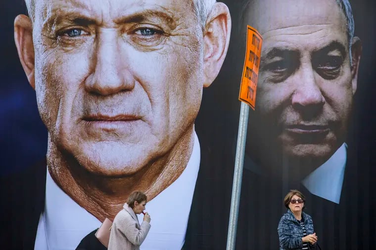 People walk by an election campaign billboard for the Blue and White party, the opposition party led by Benny Gantz, left, in Ramat Gan, Israel, Thursday, Feb. 20, 2020. Prime Minister Benjamin Netanyahu of the Likud party is pictured at right. (AP Photo/Oded Balilty)