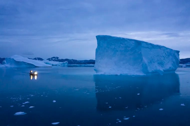 A boat navigates at night next to large icebergs in eastern Greenland in August.
