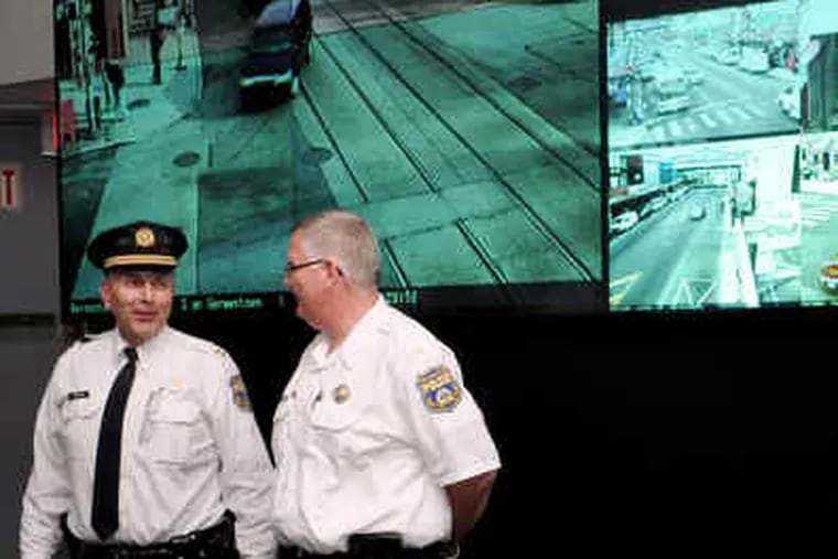 Capt. Lou Campione (left) and Lt. Tom Woltemate stand in front of the main surveillance-video screen in the Police Department's monitoring room. Police and business owners are anxious for cameras like the one at left to become operational.