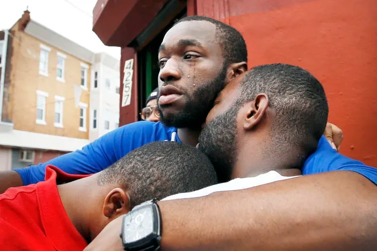 Roshawn Cox (center) comforts his brother's Jermaine Cox (left) and Jamar Cox while they hold a candle light vigil for their slain brother Terrance "Bird" Cox  in North Philadelphia.