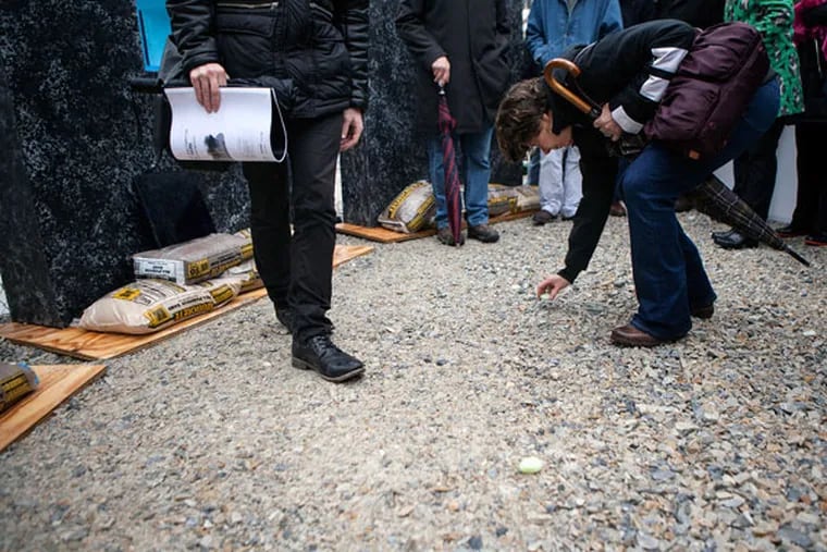 Nancy Winkler, who lost her daughter Anne Bryan in the June 2013 Salvation Army store collapse, moves a stone, signifying where one of the six people who died were found, on March 14, 2015, at 22nd and Market streets. (CHRIS FASCENELLI/Staff Photographer)
