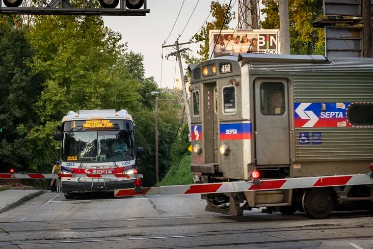 A SEPTA bus stopped at a grade crossing for an inbound Norristown Line Regional Rail train last week at School House Lane in East Falls. SEPTA has won a $15 million federal grant for new safety measures intended to prevent collisions between trains and motor vehicles at 22 highway and road crossings on five of its Regional Rail lines.