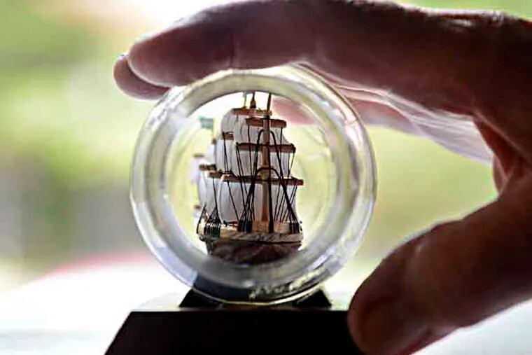 With a view looking through the glass jar opening, Joseph Ancona, a retired engineer's assistant who builds ships in bottles out of the shells of peanuts and other nuts, holds one of his creations at his Gloucester Twp. home September 26, 2013. ( TOM GRALISH / Staff Photographer )