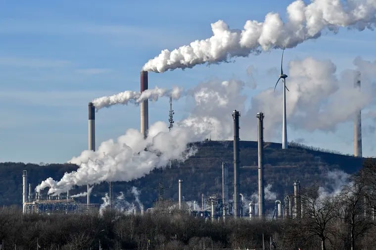 In this Jan. 16, 2020 file photo an uniper coal-fired power plant and BP refinery steam beside a wind generator in Gelsenkirchen, Germany. BP is shrinking its oil and gas business, revving up offshore wind power and developing solar and battery storage. (AP Photo/Martin Meissner)