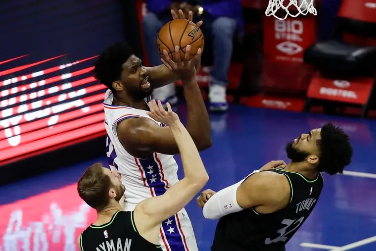 Sixers center Joel Embiid attempts to shoot against Minnesota's Jake Layman (left) and Karl-Anthony Towns in the second quarter.