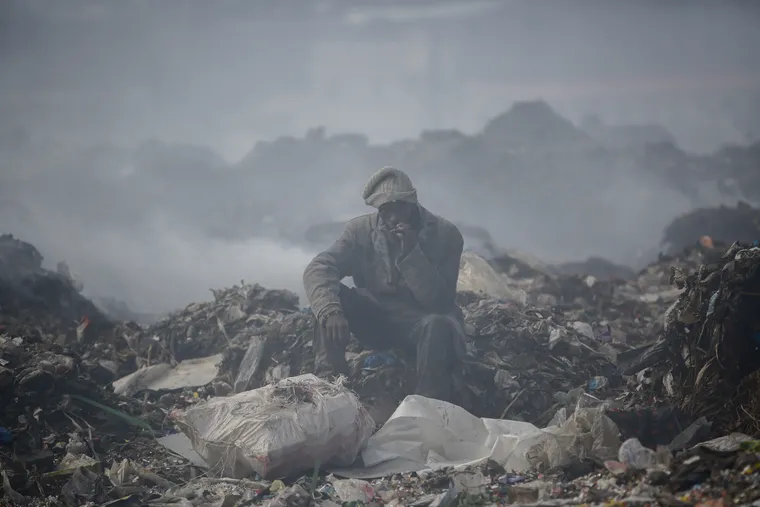 A man who scavenges recyclable materials for a living rests to smoke a cigarette on a mountain of garbage amid smoke from burning trash at Dandora, the largest garbage dump in Nairobi, Kenya.