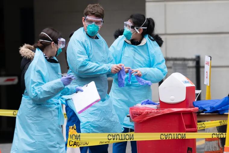 Medical workers put on gloves after washing their hands between swabbing individuals at a Jefferson Health drive-through site in Center City on March 17.