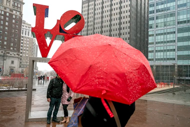 Lovers and tourists pose in front of Robert Indiana’s iconic statue as they visit LOVE Park Feb. 13, 2022 on a snowy pre-Valentine's Day.