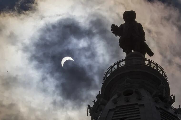 The solar eclipse can be seen beside the statue of William Penn on top of Philadelphia City Hall on Monday,
