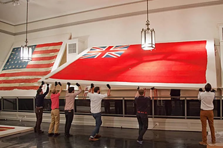 Art handlers hoist a rare English naval red ensign into place in Freeman&rsquo;s first-floor gallery. A collection of rare naval flags will be offered for sale at the auction house Monday. ELIZABETH FIELD / Freeman&rsquo;s