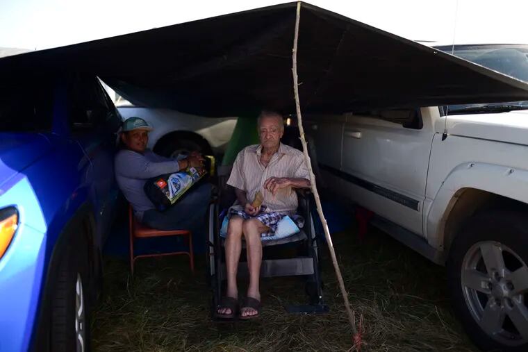 In this Friday, Jan. 10 photo, residents from the Indios neighborhood of Guayanilla, Puerto Rico, Milagros Figueroa and Ruben Fantausi, sit under a tarp between vehicles parked on a private hay farm where locals affected by earthquakes have set up shelter amid aftershocks in Guayanilla, Puerto Rico. A 6.4 magnitude quake that toppled or damaged hundreds of homes in southwestern Puerto Rico is raising concerns about where displaced families will live, while the island still struggles to rebuild from Hurricane Maria two years ago.
