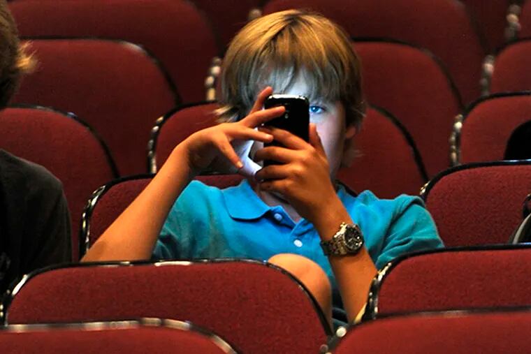 Haddonfield Memorial HS freshman Ryan Meyer, 14, uses his smart phone as his school becomes the latest to take on a new weapon against cyberbulling, in the auditorium September 11, 2104. Earlier in the morning he and his classmates attended a rally to celebrate and to learn more about the weapon - an app called  STOPit, created by a Jersey man after hearing about a Canadian girl who killed herself due to cyberbullying. ( TOM GRALISH / Staff Photographer )