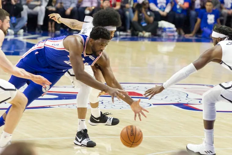 Joel Embiid, left, of the Sixers dives after a loose ball against Jarrett Allen, center, and DeMarre CArroll of the Nets during the 1st half of their NBA playoff game at the Wells Fargo Center on April 13, 2019.