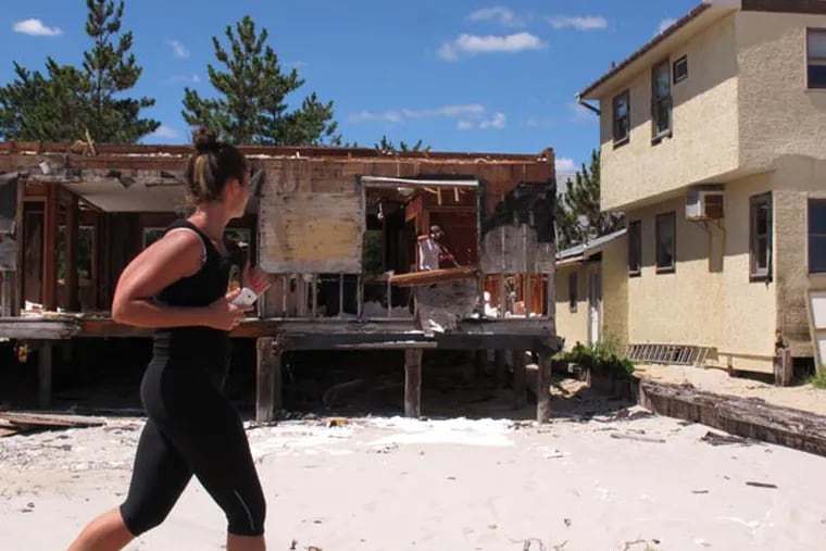 In this Aug. 14, 2013 photo, a jogger watches as a man cleans out the remains of a home on the Lavallette, N.J., beachfront that was gutted by Superstorm Sandy. A group of storm victims who still cannot return to their damaged homes appealed to New Jersey lawmakers for help during a public hearing in Atlantic City on Thursday, Aug. 15, 2013. (AP Photo/Wayne Parry)