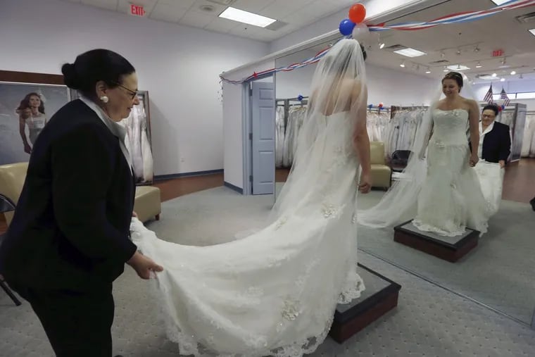 Store employee Jo Acchione helps as former Army National Guard member Jennifer Dunn tries on a wedding gown at Alfred Angelo Bridal in Cherry Hill in 2015.,