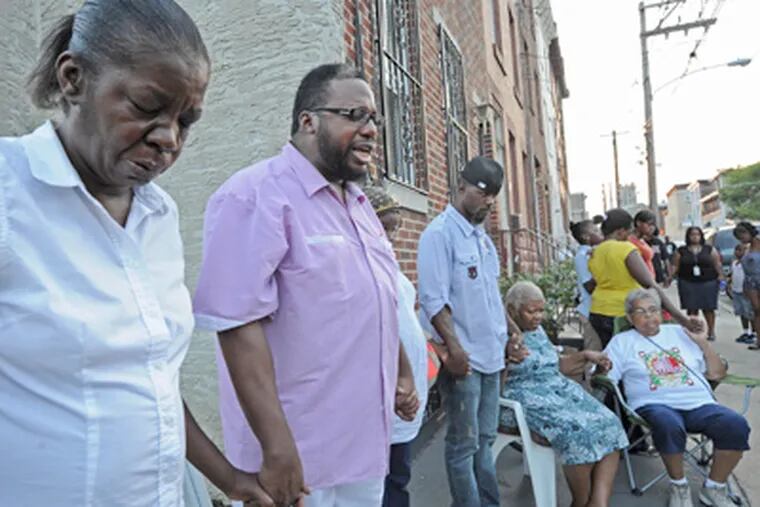 On West York Street in North Philadelphia, friends of James "Bus" Hall pray. At left is Hall's girlfriend, Juanita Johnson; next to her is Pastor Glenn Dawson of the Evangelistic Temple Worship Center. (April Saul / Staff Photographer)