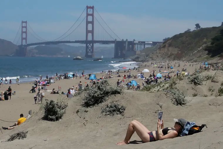 Sara Stewart read a book while maintaining a safe distance from crowds visiting Baker Beach in San Francisco last weekend.