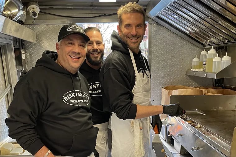 Actor Bradley Cooper (right) works on the Danny & Coop's cheesesteak truck with Angelo's Pizzeria owner Danny DiGiampietro (left) and manager Seth Braunstein in New York on Dec. 6, 2023.