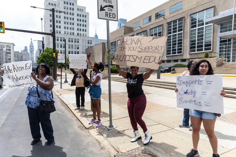 Many gather holding signs as Constance Jones, 30, of Mount Airy, Pa., is on the speaker phone, asking the school district to supply resources for students and family members with autism outside of the School District building in Philadelphia, Pa., on Friday, April 22, 2023.