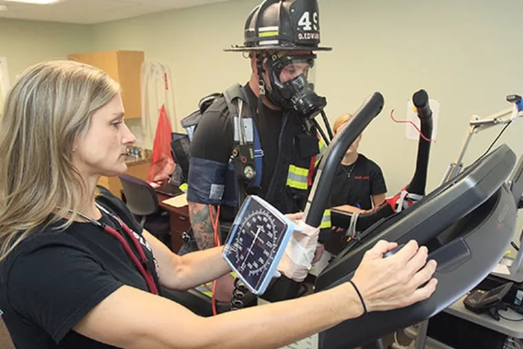 Deborah Feairheller, left, has a Ph.D.in exercise physiology and sports science and teaches at Ursinus College. The Penn State grad and mother of three also is a volunteer firefighter. She performs a test on Dane Edwards, 23,  a firefighter in full uniform, walking on a treadmill.