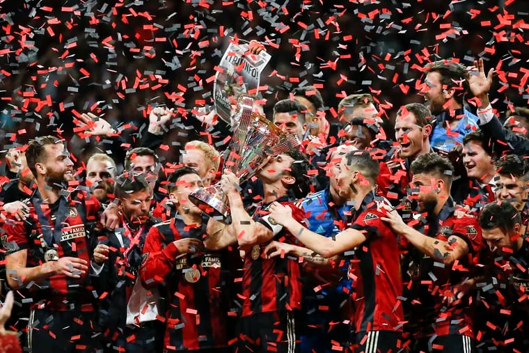 Atlanta United team captain Michael Parkhurst (3) kisses the trophy as teammates celebrate during the trophy presentation after the MLS Cup championship soccer game against the Portland Timbers, Saturday, Dec. 8, 2018, in Atlanta. Atlanta United won 2-0. (AP Photo/Todd Kirkland)