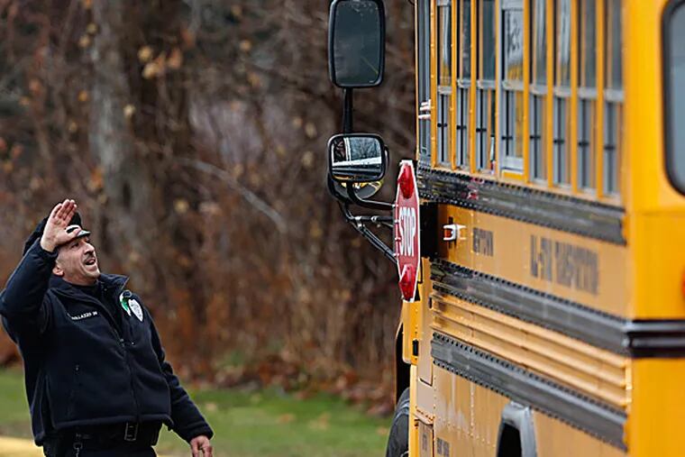 Easton police officer J. Sollazzo waves to returning children as their bus pulls into Hawley School on Tuesday in Newtown, Conn. Classes resume Tuesday for Newtown schools except those at Sandy Hook. JASON DeCROW / Associated Press