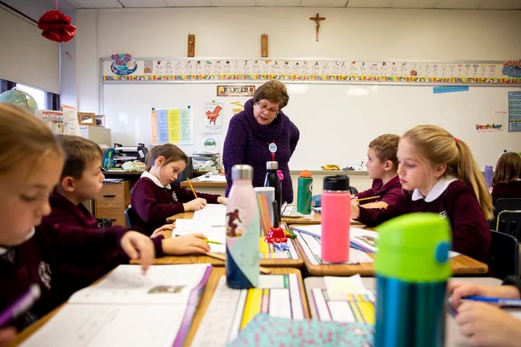 Lori Carrozza, second-grade teacher at Cardinal John Foley Regional Catholic School, helps her students and guides them to write the letter k in cursive during class on Wednesday, Dec. 11, 2019. The pandemic has threatened the finances of Catholic schools in the region.