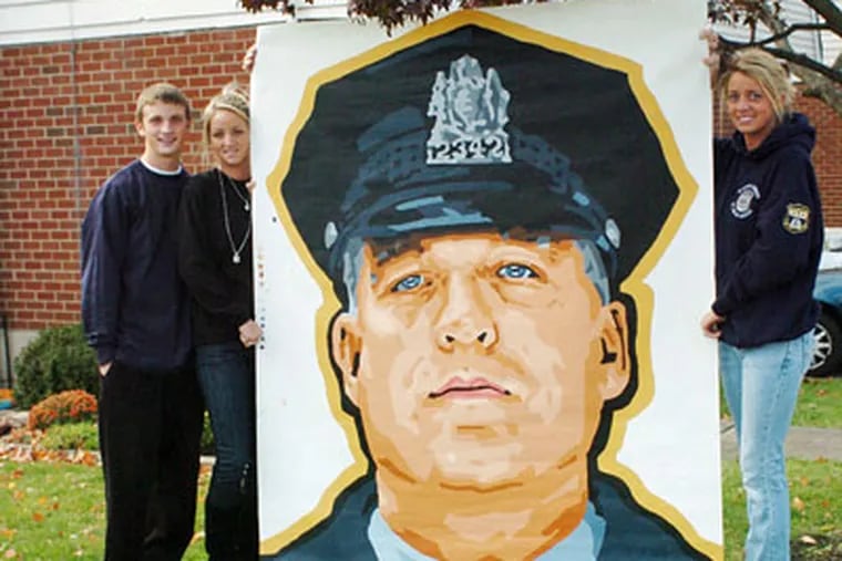 Posthumous tributes to Officer Cassidy have been many. Above, his children - John and Colby on the left, Katie on the right - hold a mural-sized portrait of their father in October 2008. (Jessica Westergom / Staff Photographer)