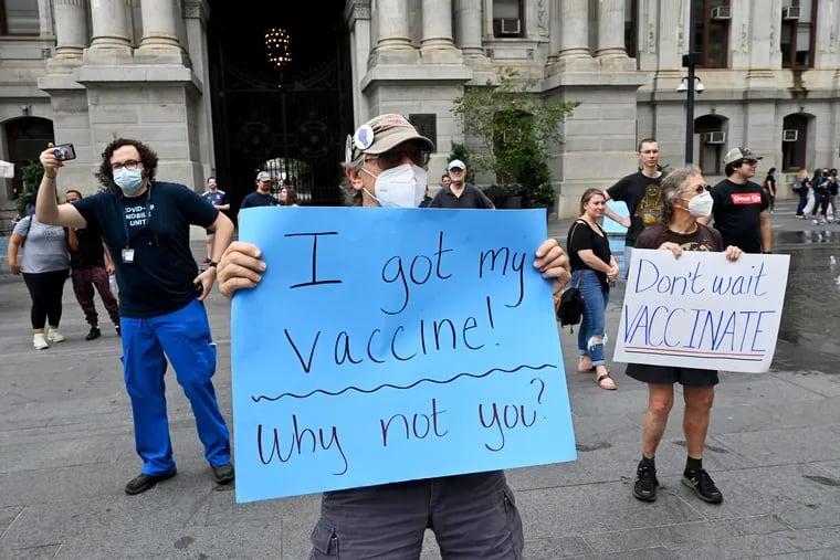 At August's Vax Up Philly parade at City Hall, Hans Peters (center) and Laura Lynch of Bucks County couple hold signs promoting vaccination. Clinical pharmacist Robert Pugliese (left), co-director of Jefferson University Hospitals' Mobile Community Vaccination Program and director of innovation design, photographs the scene.