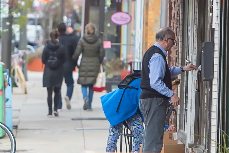 A shop owner on Passyunk Avenue in South Philadelphia wipes off the door handles of his business after locking the doors on Monday, March 16, 2020, at 5 p.m. in compliance with Philadelphia Mayor Jim Kenney's directive on non-essential businesses having to close due to the coronavirus.