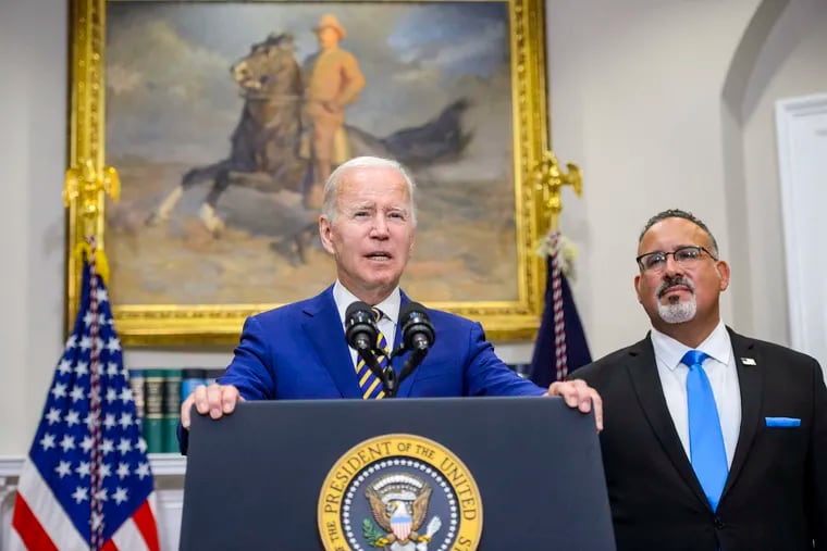 President Joe Biden speaks as Secretary of Education Miguel Cardona looks on during an event to announce a federal student loan relief plan at the White House on Aug. 24, 2022.